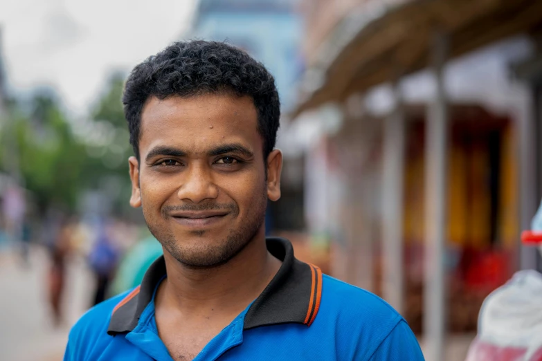 a man smiling in front of a street with buildings in the background