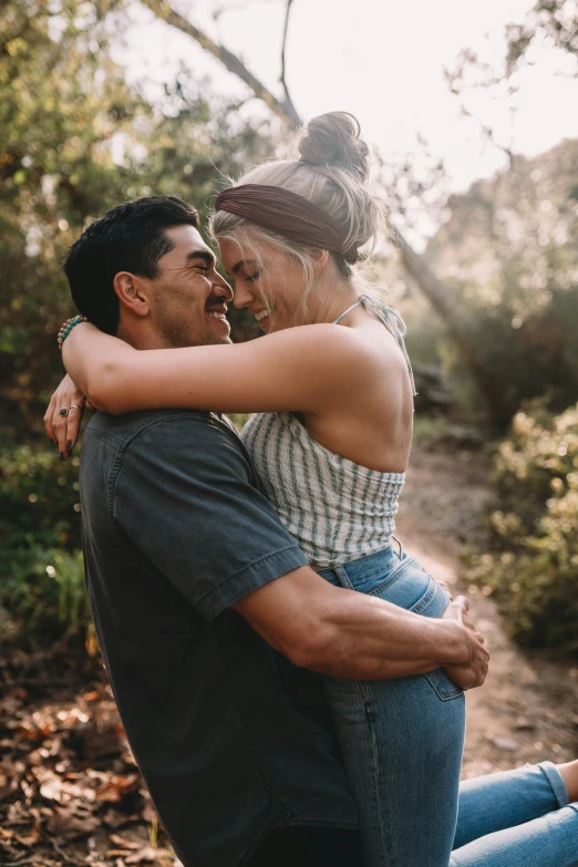 the woman and man hug each other by a forest