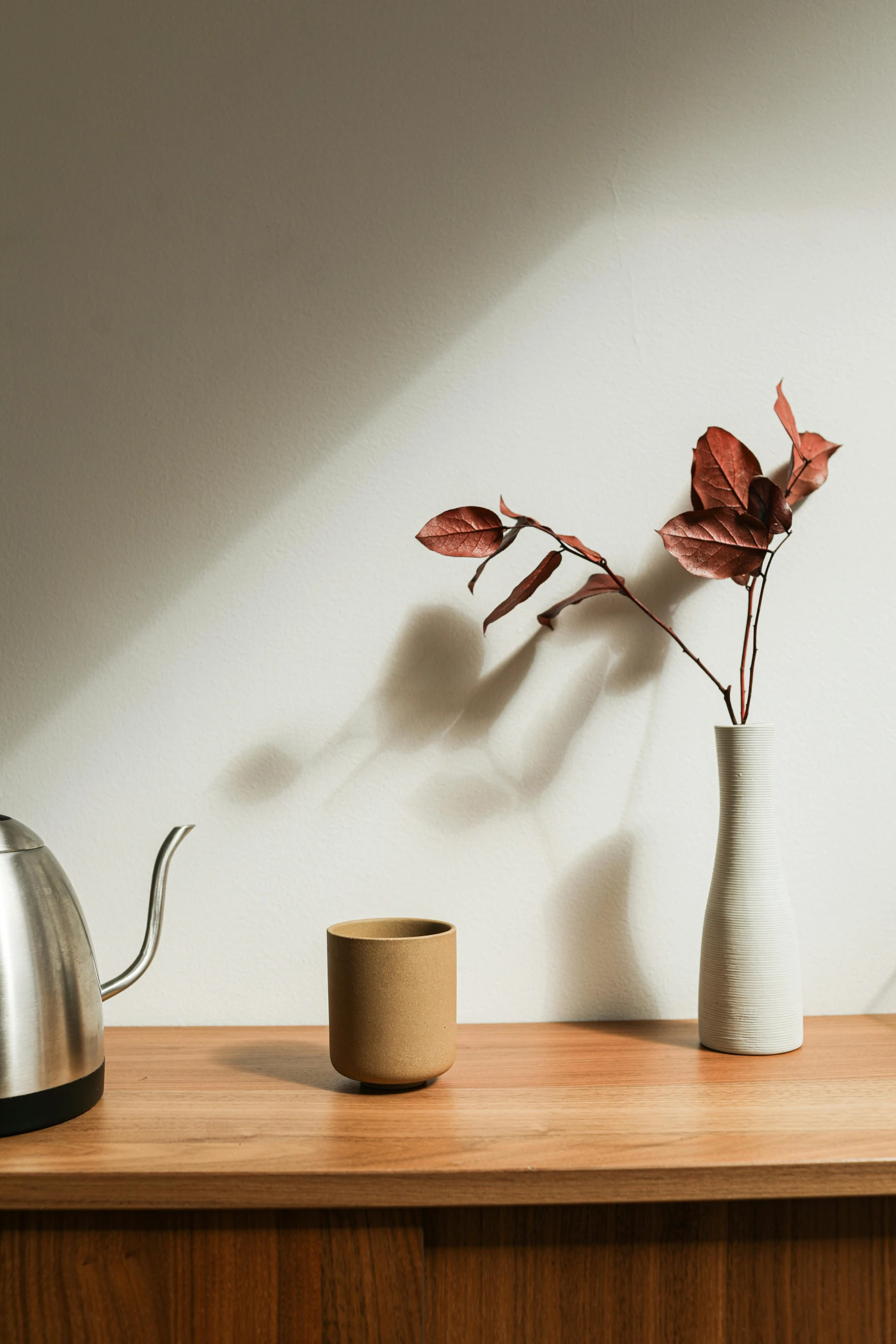 there is a vase with leaves in it, next to the tea kettle and coffee pot