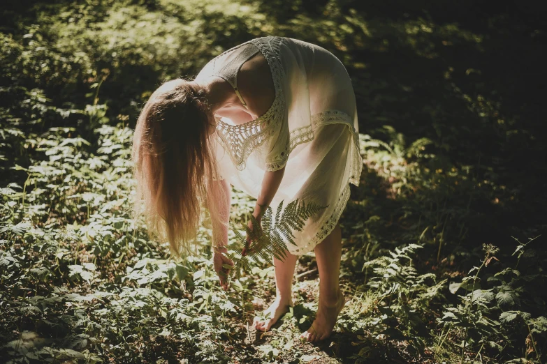 a woman is bent over by a tree in a forest