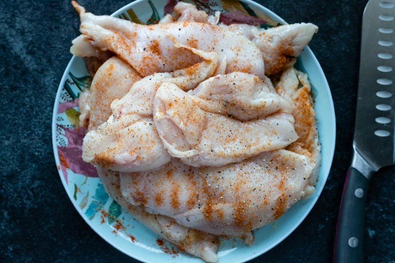 meat is covered in spices and seasonings on the plate next to a knife