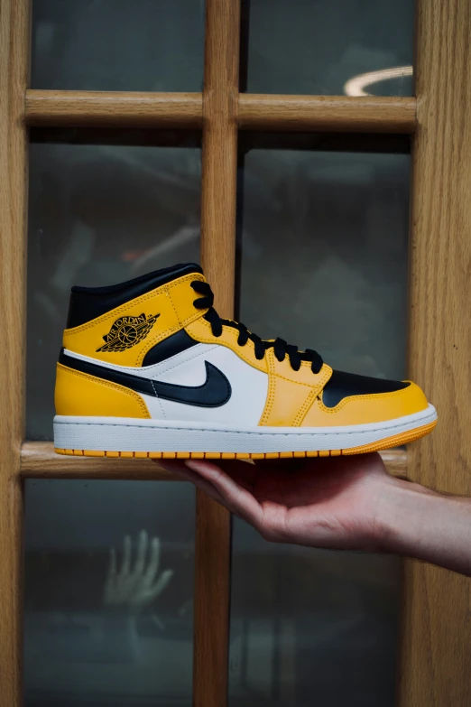 a hand holding up a yellow and black nike shoe
