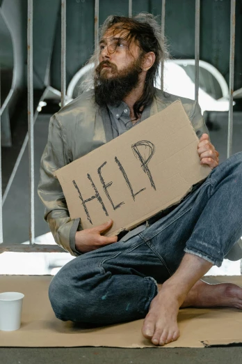 a homeless man sitting on a step holding a cardboard sign reading help