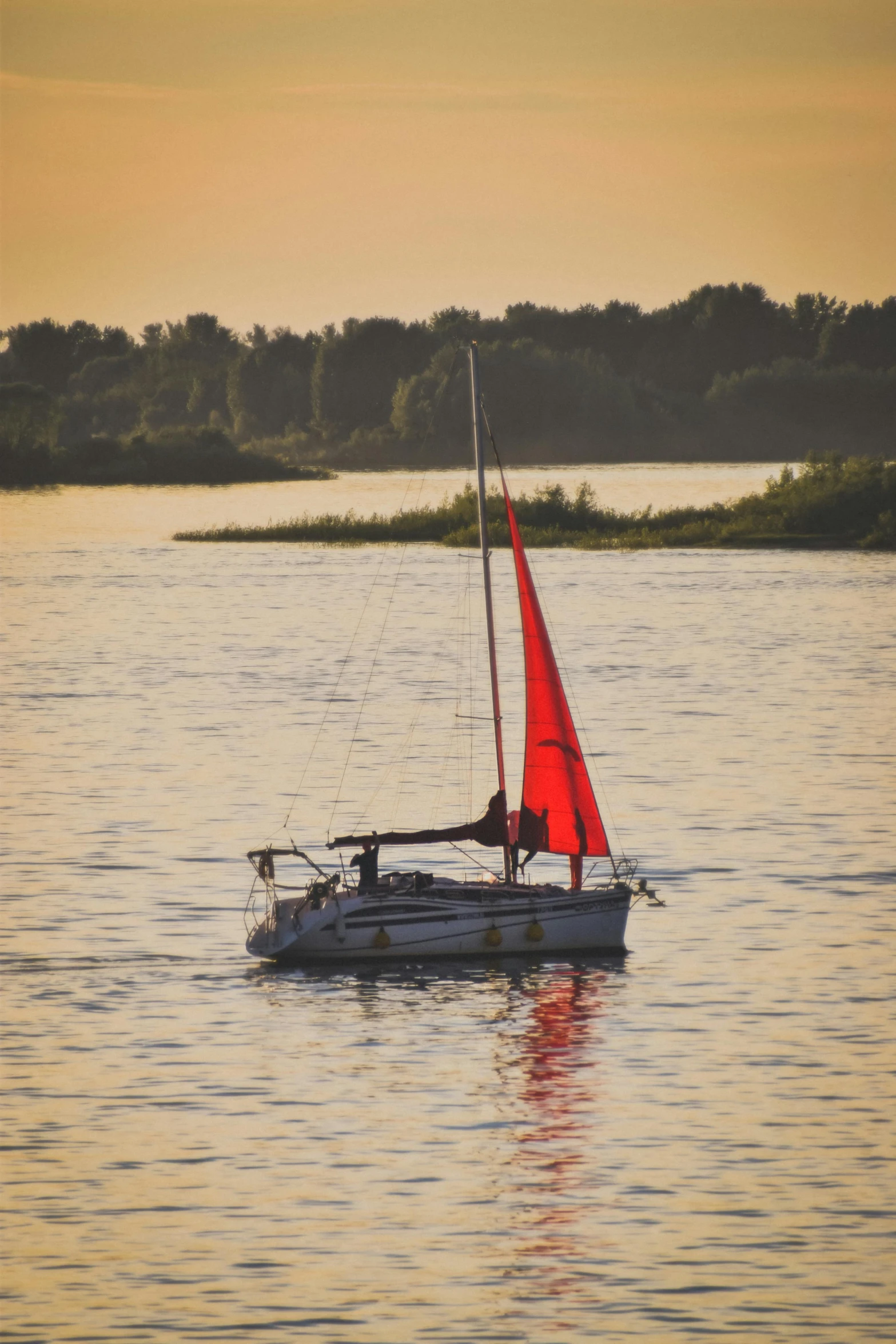 a red sailboat floats through the water at dusk