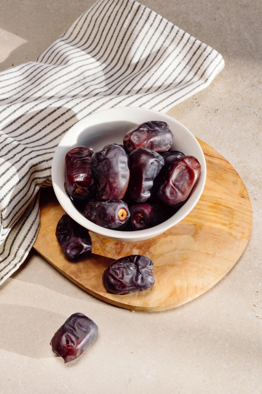 a bowl of plums are sitting on a  board with a white and blue striped napkin