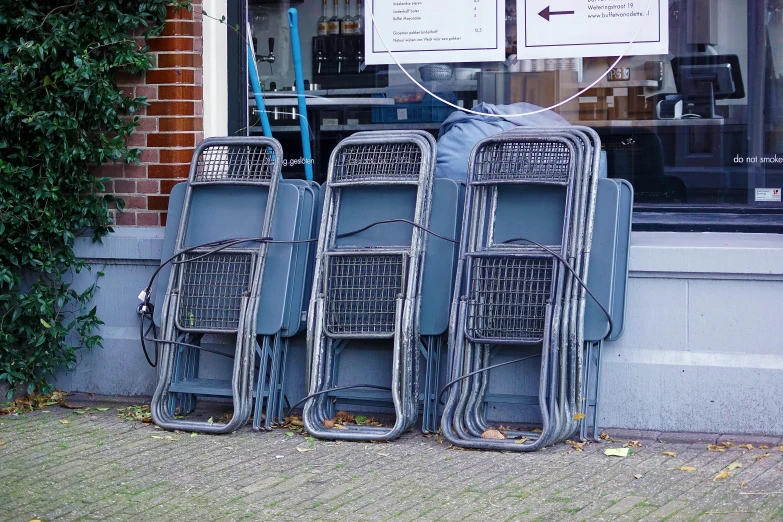 three metal chairs leaning against a wall outside a store