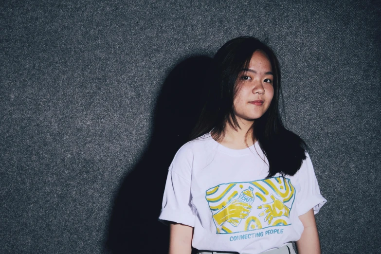 a young asian woman wearing a tshirt standing in front of a wall