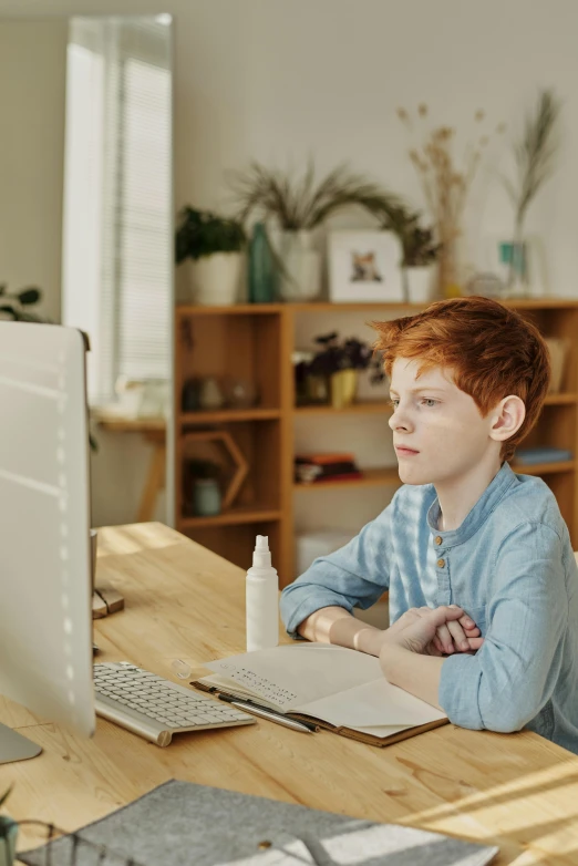 a child with a messy red hair looks at soing on a desk