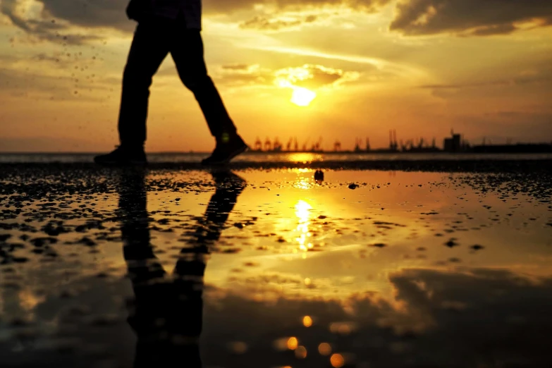 a man walks with his feet in the water while sun sets