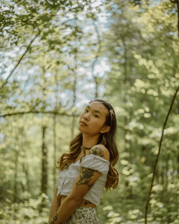 a young woman stands in the woods with trees behind her