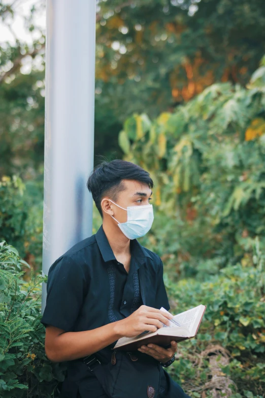 a man wearing a mask reading a book next to a street light