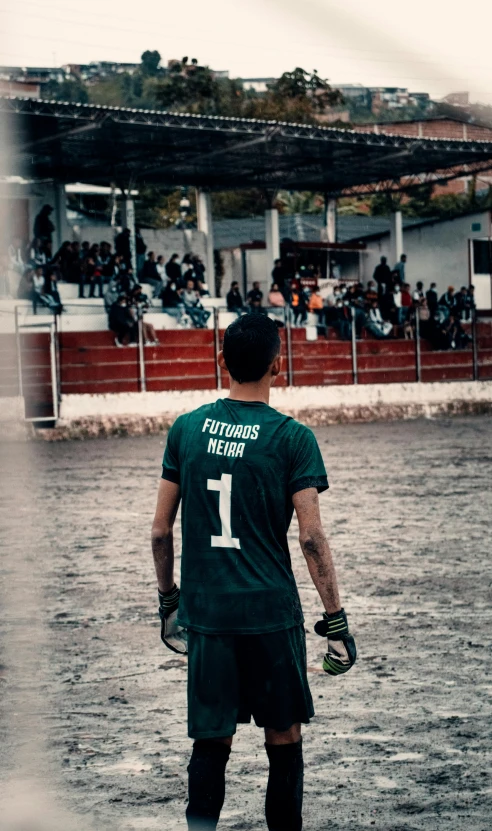 a man in a green soccer uniform stands on a rainy field