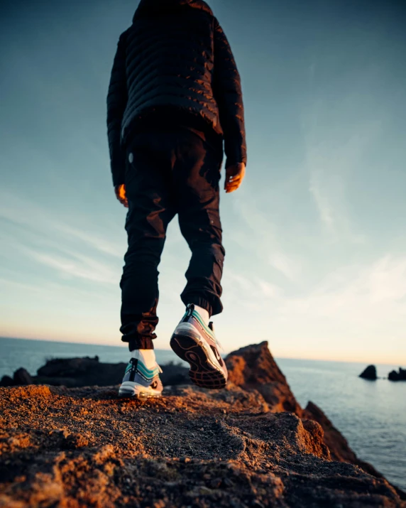 a person in white sneakers stands on rocks overlooking the ocean