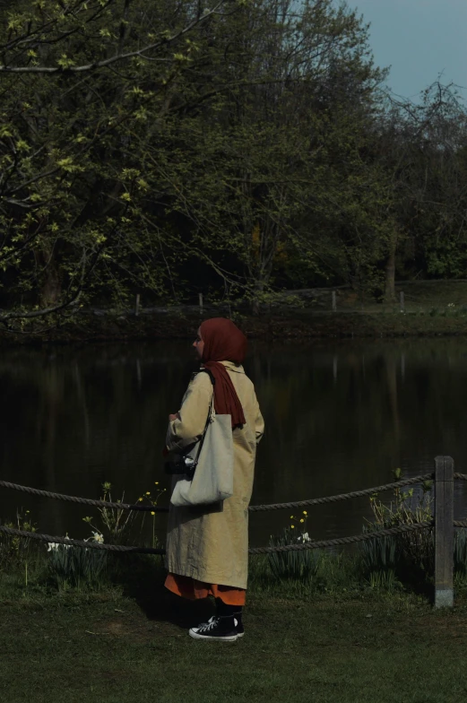 a woman is standing in front of a lake, watching soing from the park