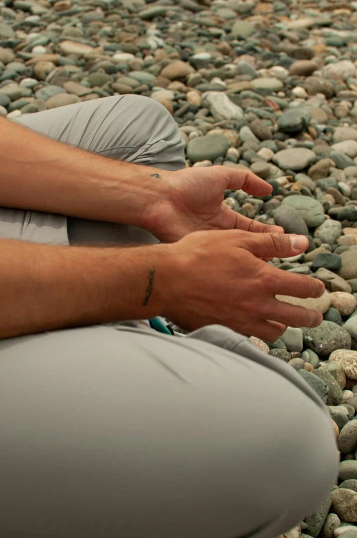 a man is seated on a bed of rocks holding his hands together and there are two fingers touching the ground