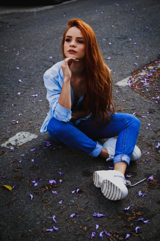 a beautiful woman sitting on the ground holding her chin in one hand