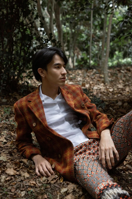 a man in patterned pants and jacket sitting on leaves