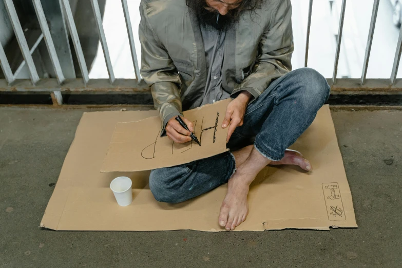 a man with glasses sitting on a cardboard box holding a marker