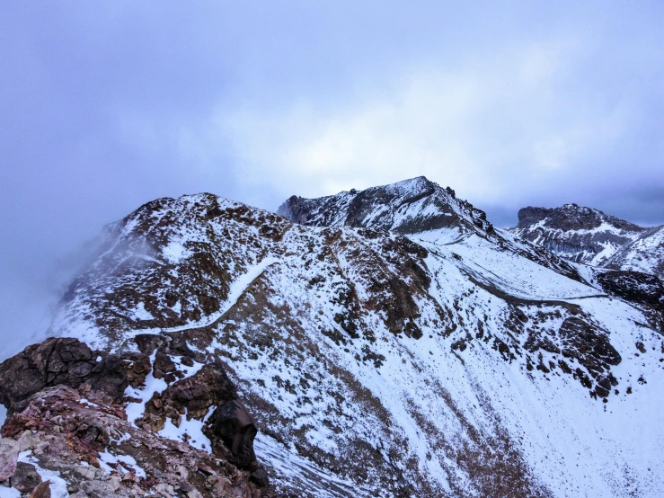 a snow covered mountain has some clouds above it