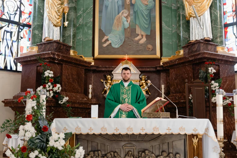 a priest standing behind an alter, wearing green robes