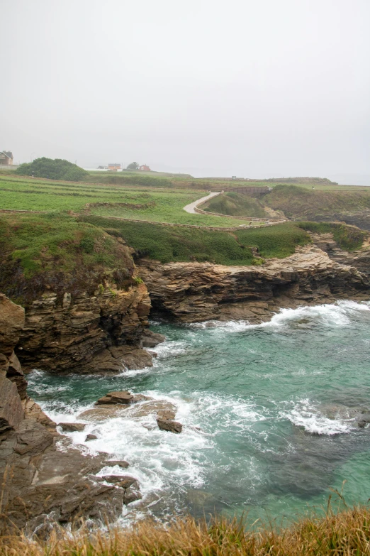 waves crashing on a beach next to a grassy coast