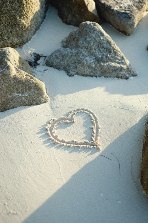 a heart drawn in sand next to rocks