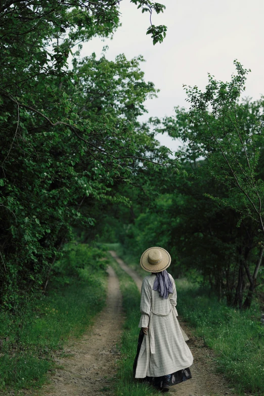 a woman in a long white coat and hat is walking down a dirt road