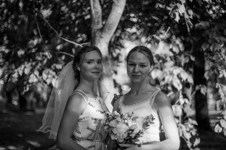 two women in gowns and veils stand under a tree