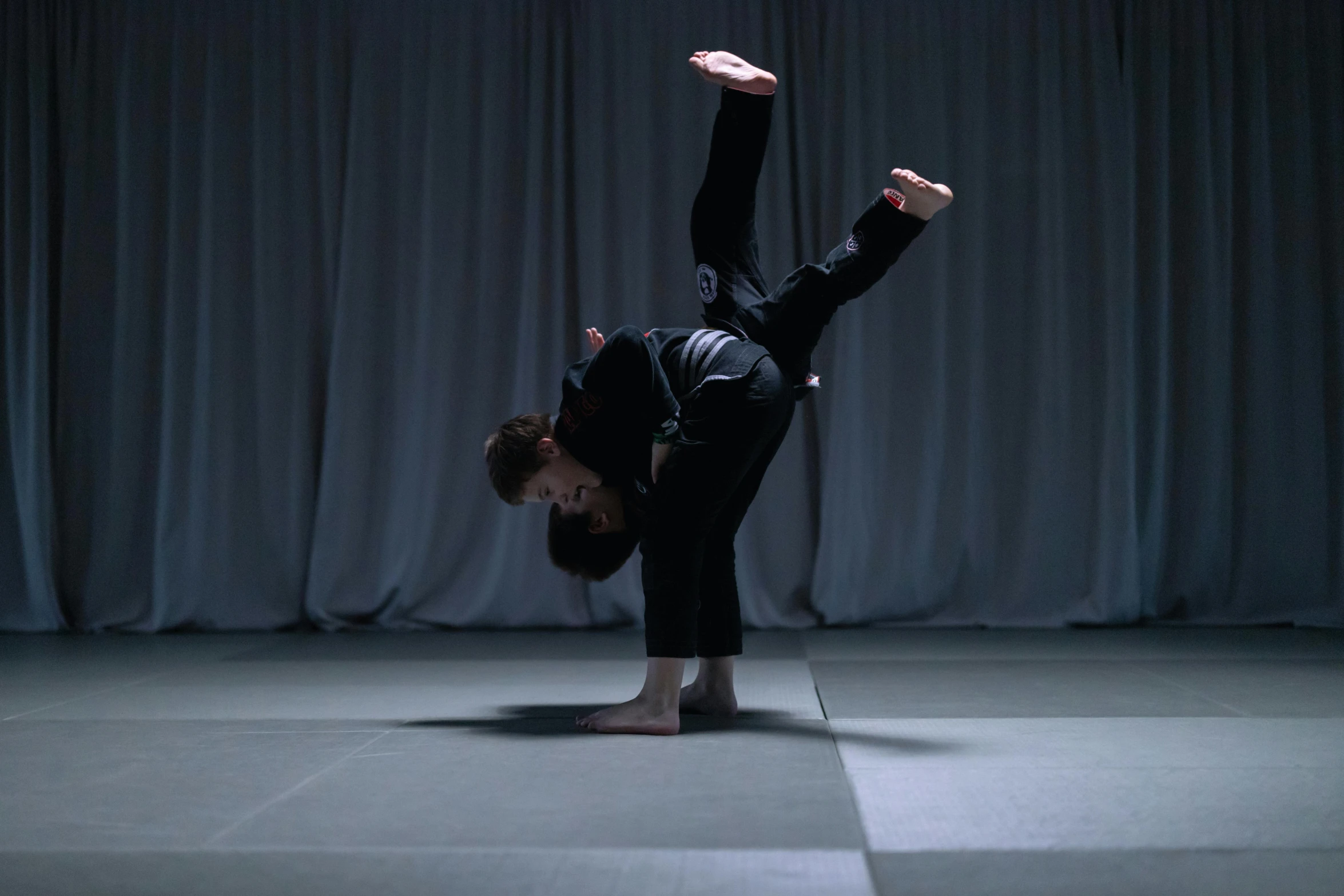 a person in a black outfit does a handstand on a floor with white squares