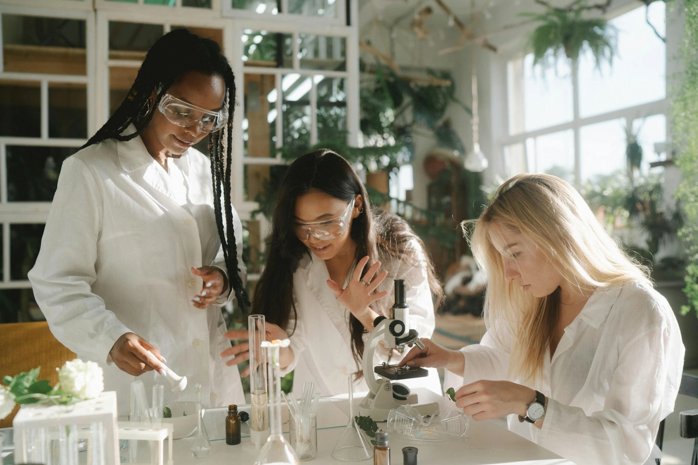 three girls in lab coats looking through microscopes at flasks