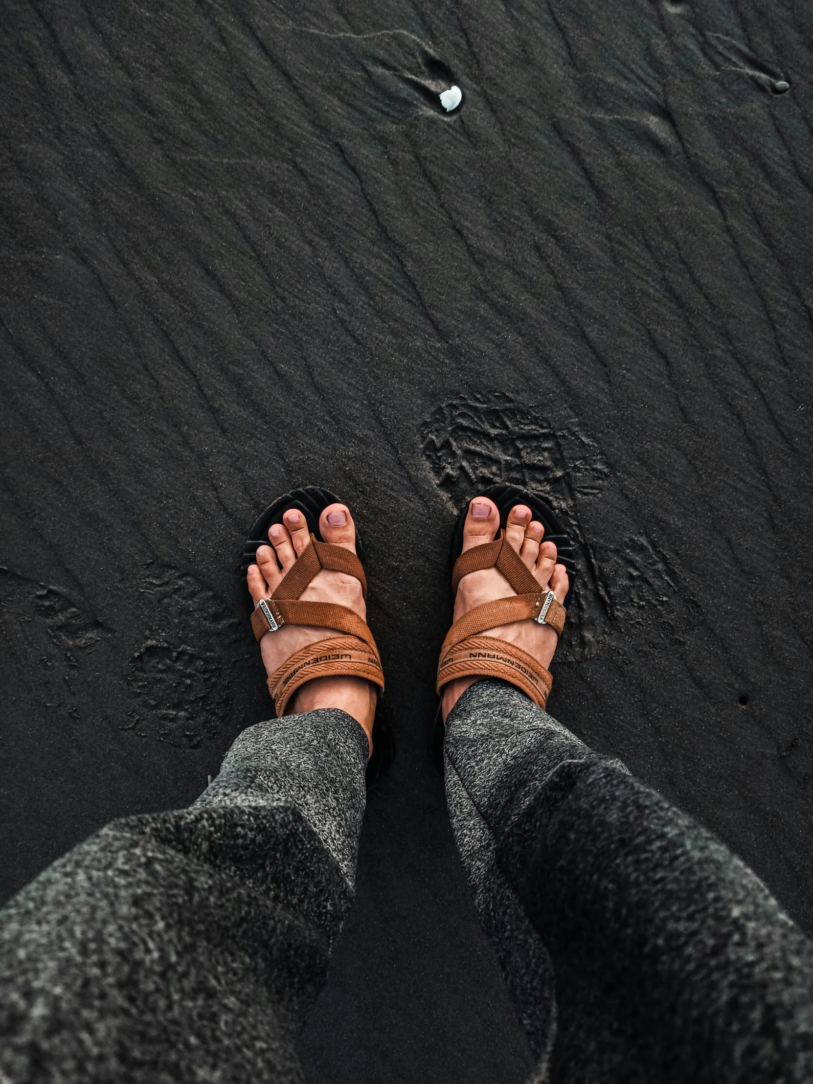 person with a pair of sandals, standing on black sand