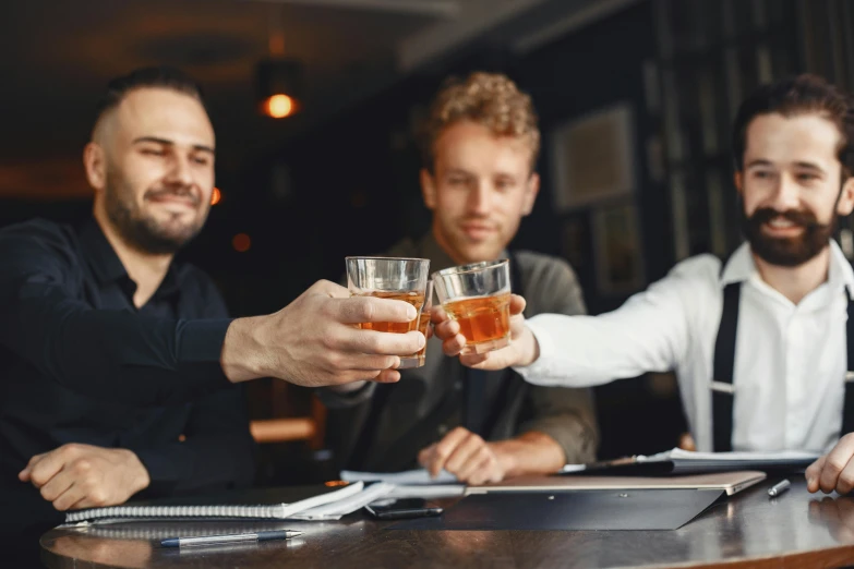 a man holding two glasses while sitting at a bar