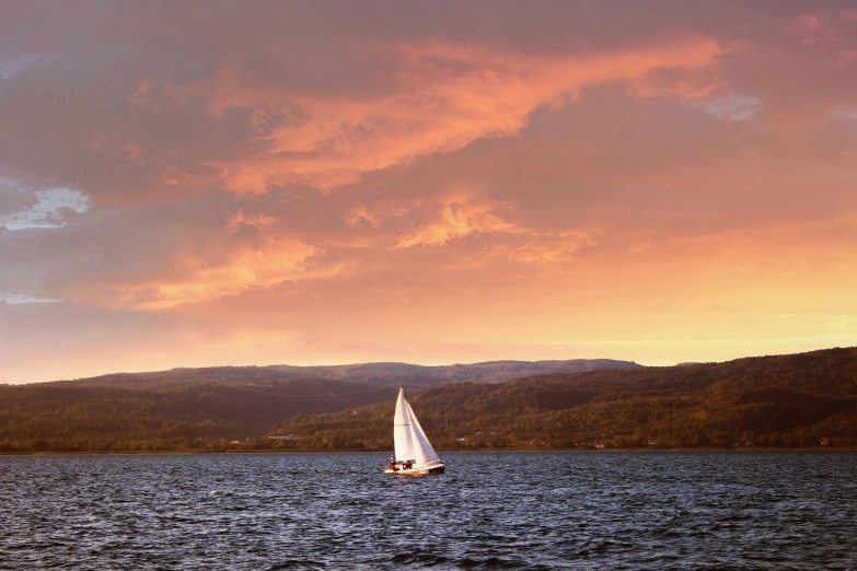 a sail boat sailing across a body of water under a cloudy sky