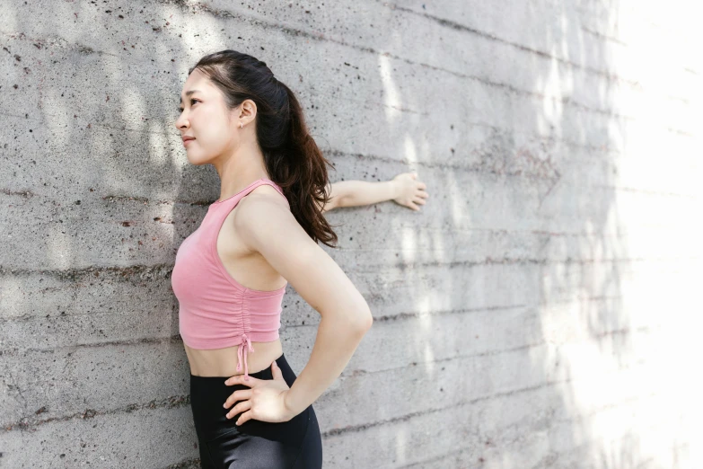 a woman wearing a pink top is leaning against a brick wall