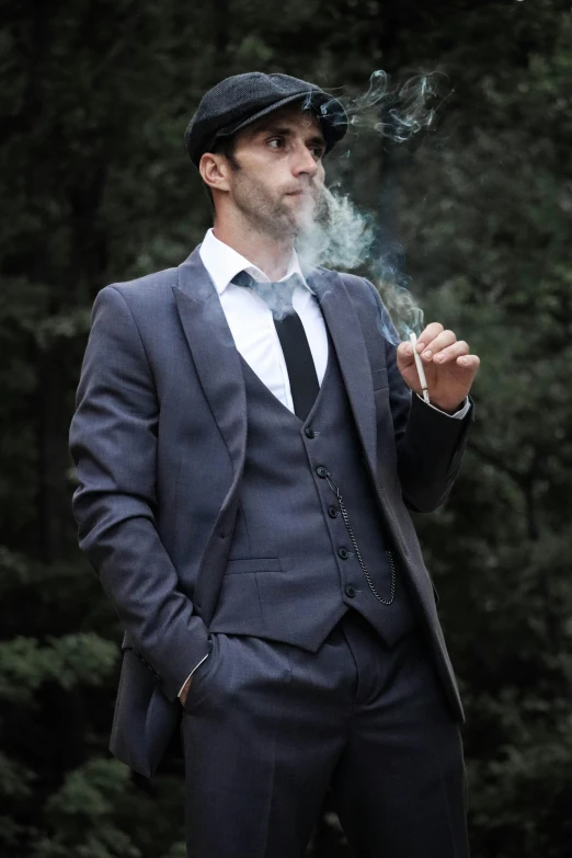 a man in a suit smokes a cigarette in front of trees