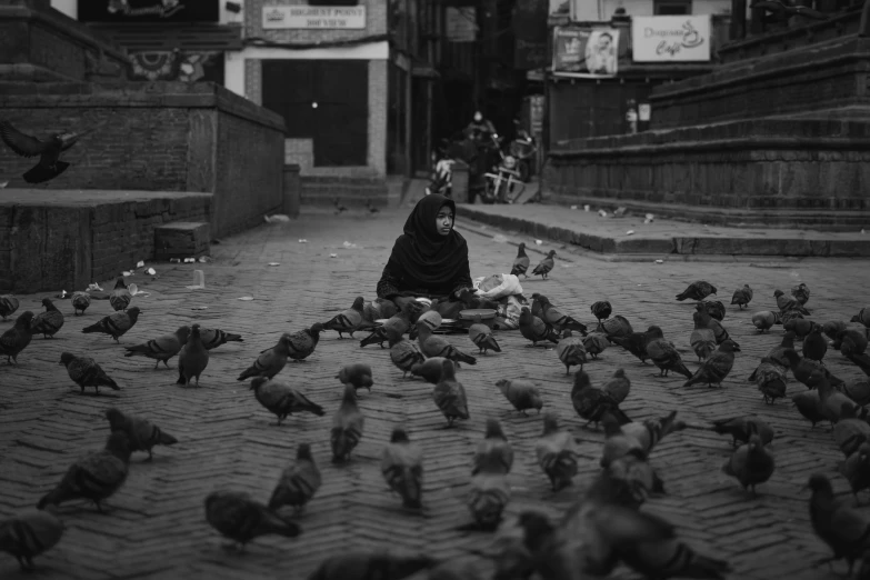 the girl is sitting on the street with many birds
