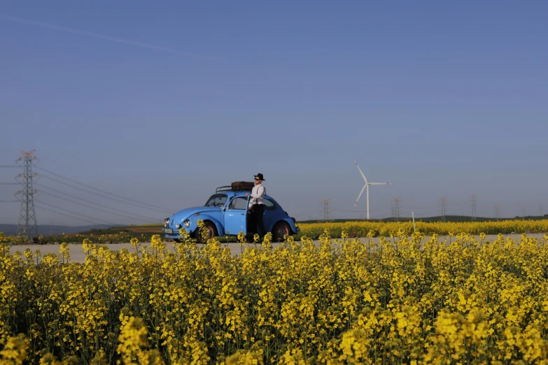 man stands beside small car with windmill in the background