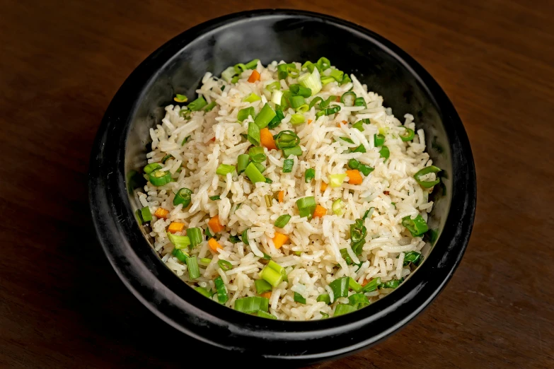 a rice dish in a black bowl on a wooden table