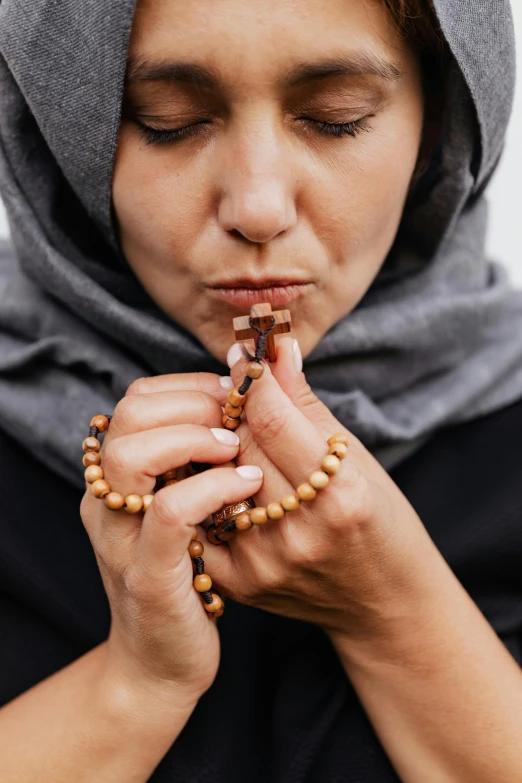 a woman in a hood and head scarf is holding a wooden rosary