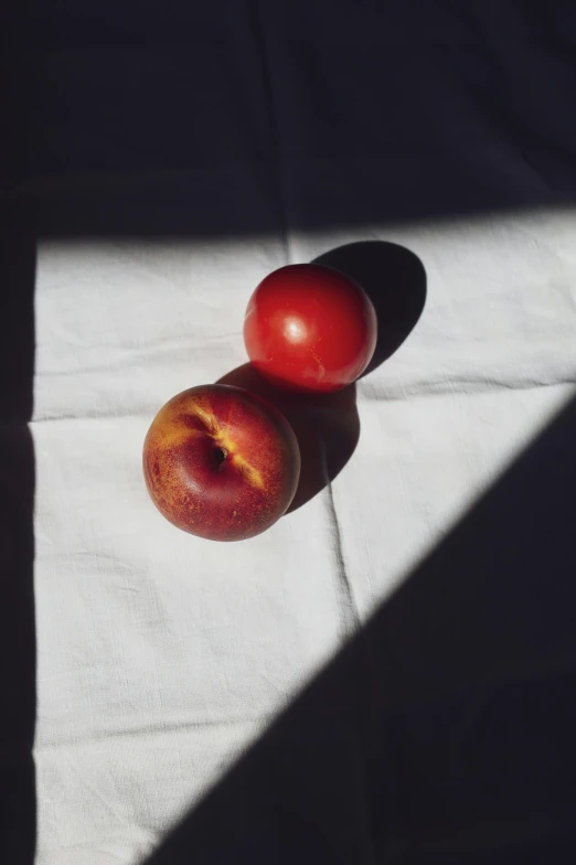 two tomatoes sit on a cloth near a pair of small peaches