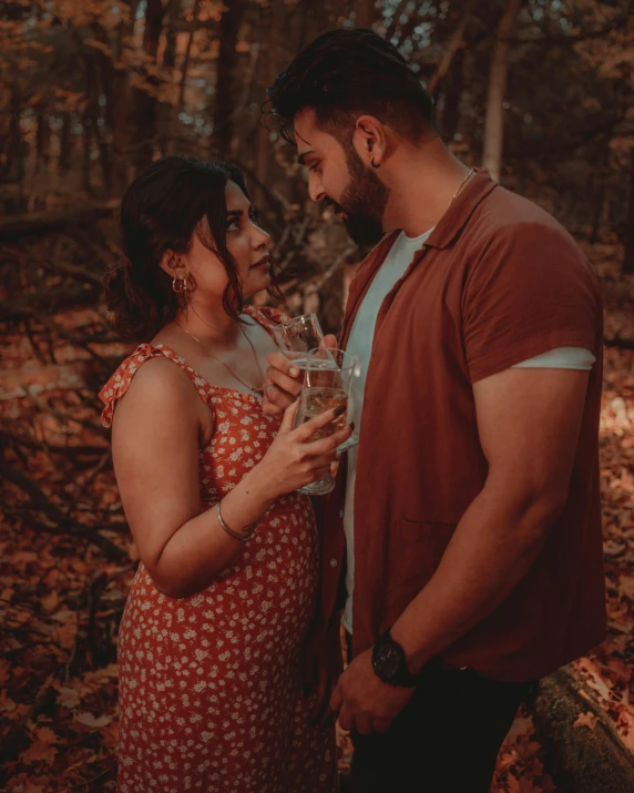 a young man and woman stand in a forest with leaves on the ground