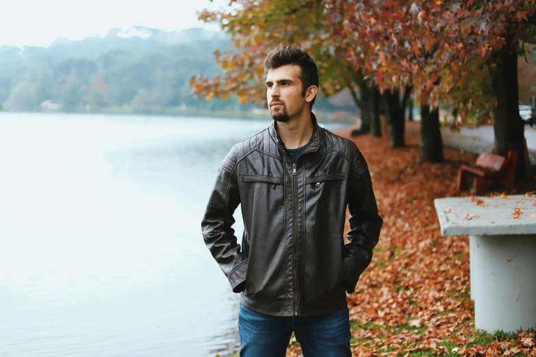 man standing near water during autumn near bench