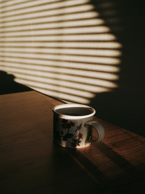 a mug on the ground with the shadows of lines from the blinds