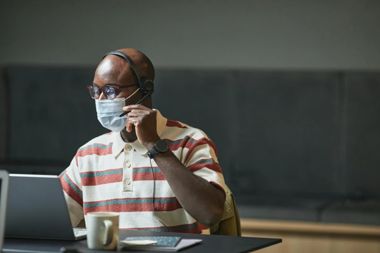 a man in glasses wearing a face mask on his right side while using a laptop