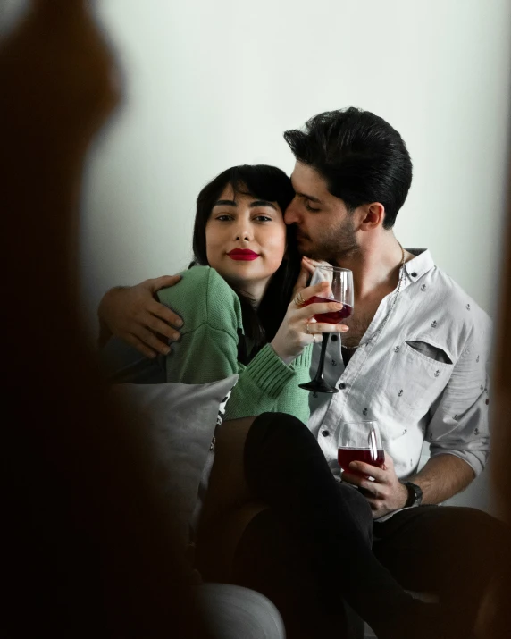 a man and woman sitting on a couch cuddling and drinking wine