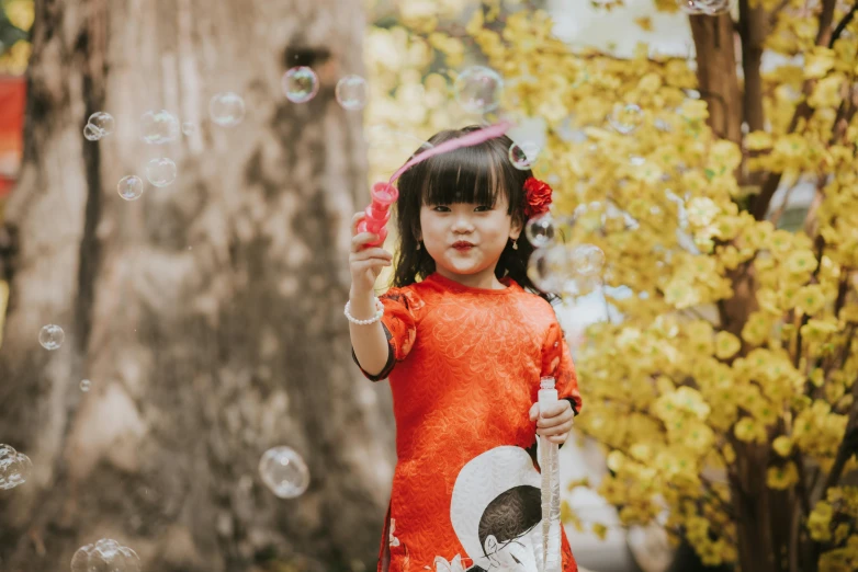 a little girl in red dress holding up a soap bubble