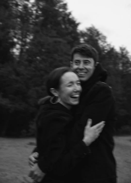 a man and woman hug in a park by trees