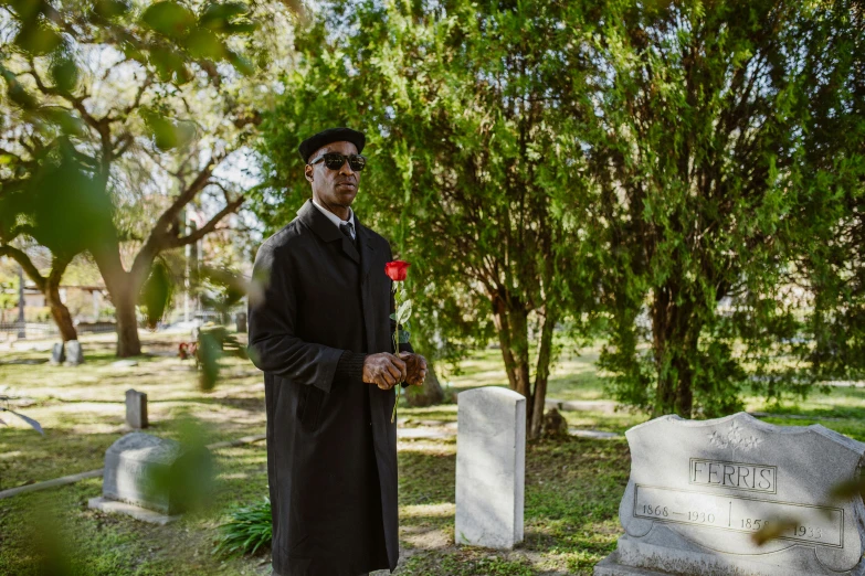 a man in black suit holding a red flower at the grave