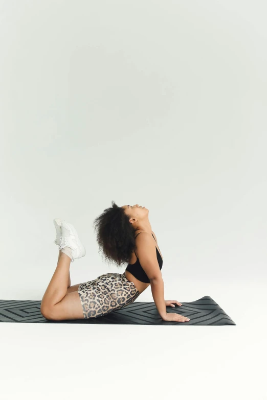 a woman with dark hair, wearing leopard print leggings and black tank top, leaning on a cheetah pattern towel