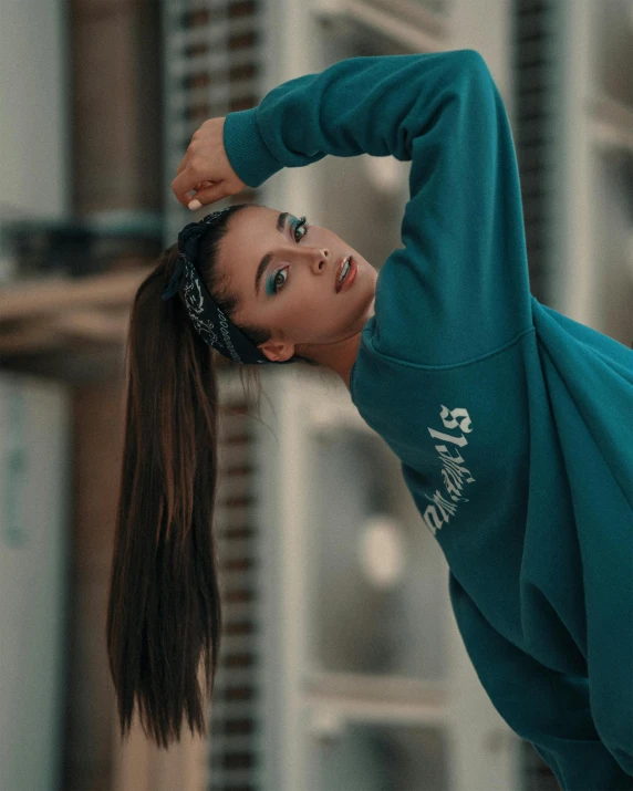 an attractive woman in a turquoise sweatshirt leaning on the wall